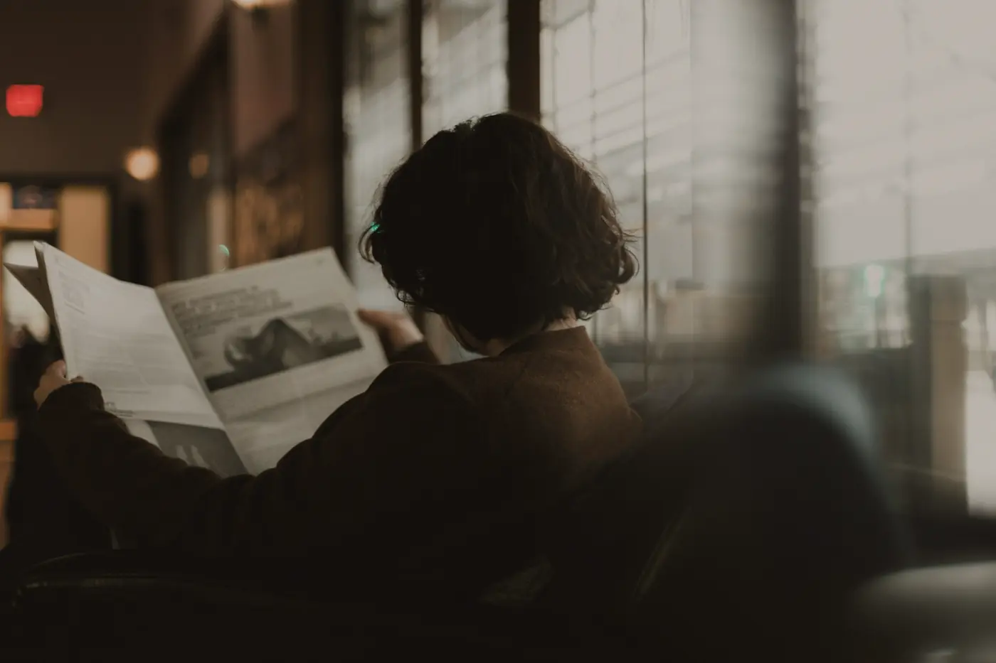 Lectrice absorbée par son journal près d'une fenêtre