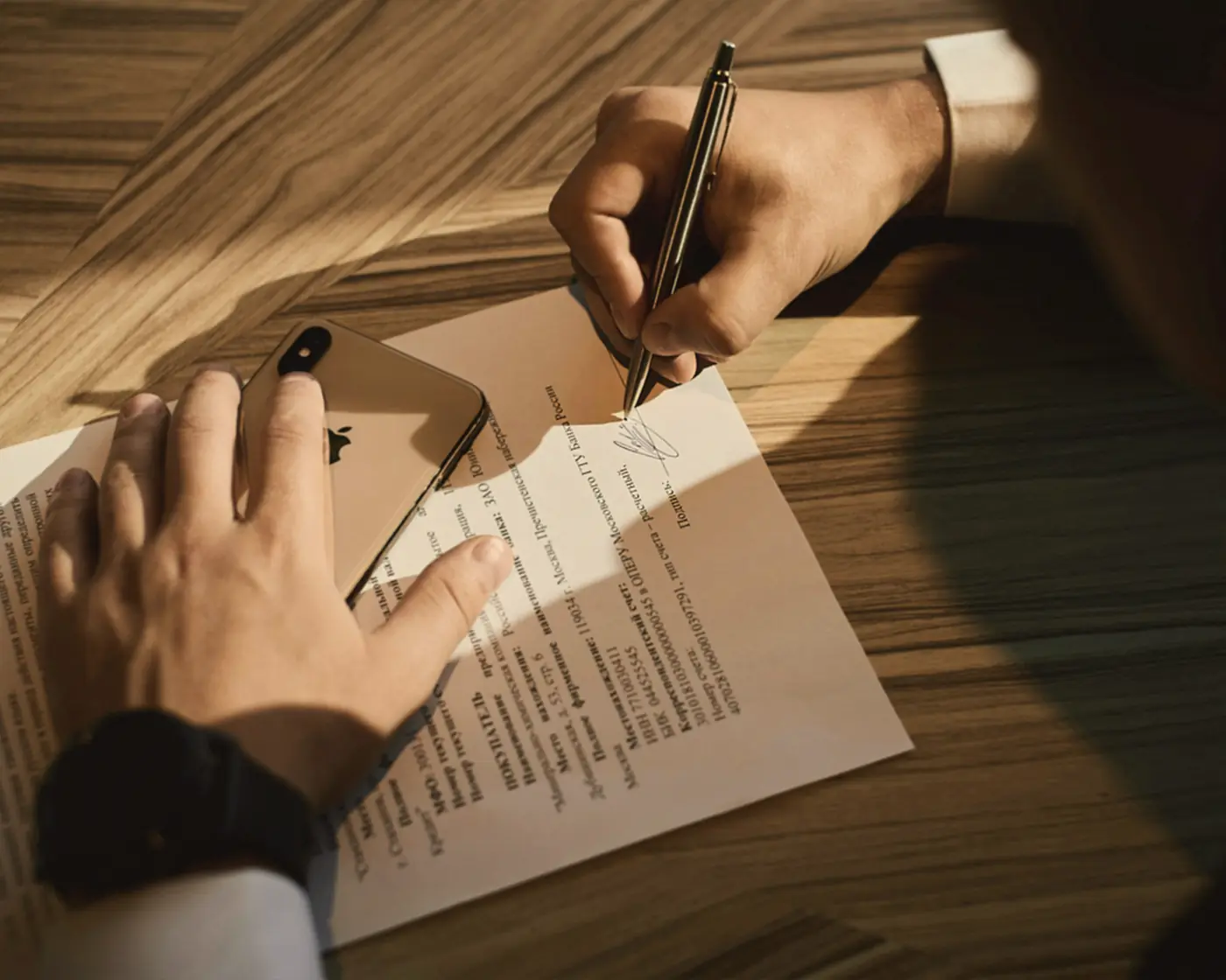 Main signant un acte sur un bureau en bois, lumière rasante