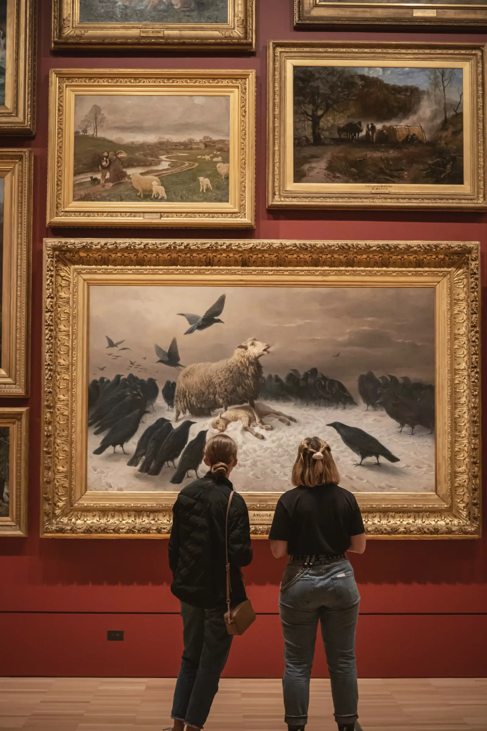 Deux visiteuses devant des tableaux anciens accrochés sur un mur rouge